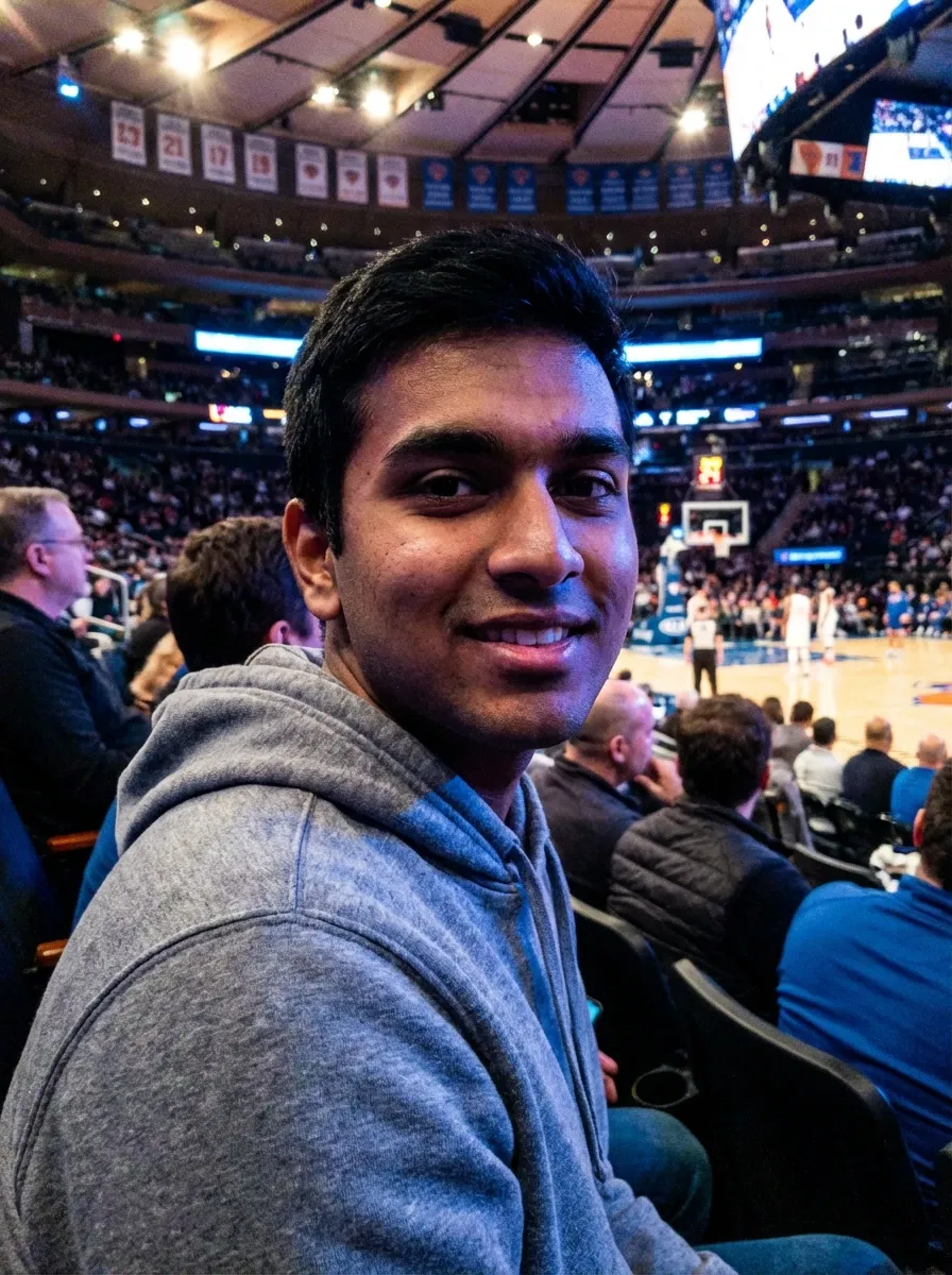 Arena photo of a man in a gray hoodie seated at a basketball game